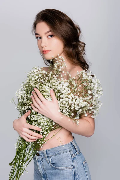 Shirtlose brünette Frau mit kleinen weißen Blüten, die in die Kamera schaut, isoliert auf grau — Stockfoto
