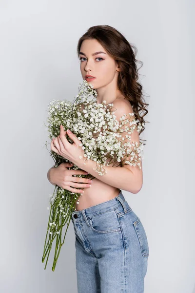 Shirtless woman holding baby breath flowers and looking at camera isolated on grey — Stock Photo