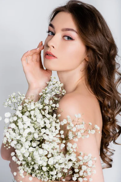 Donna con spalla nuda e mano vicino al viso che tiene fiori isolati su grigio — Foto stock
