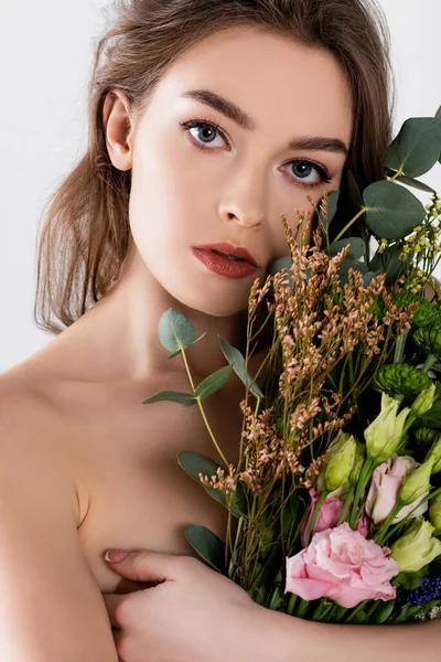 Mujer sin camisa mirando a la cámara mientras abraza flores aisladas en gris - foto de stock