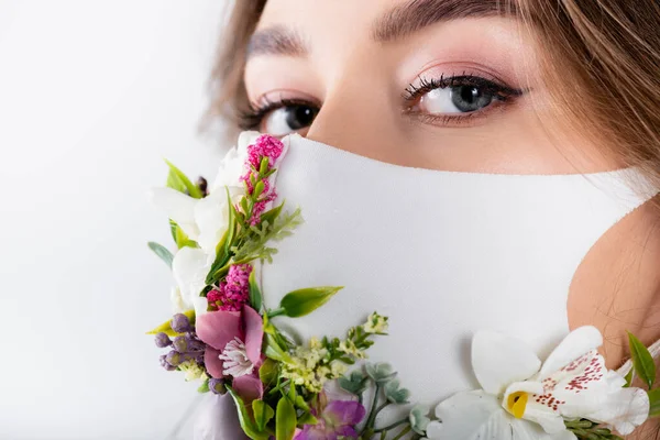 Donna in maschera medica con fiori guardando la fotocamera isolata su bianco — Foto stock