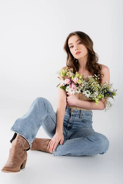 Модна модель з квітами в блузці дивиться на камеру, сидячи на сірому фоні — стокове фото
