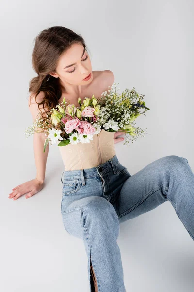 Vista aérea de mujer morena con flores en blusa sentada sobre fondo gris - foto de stock