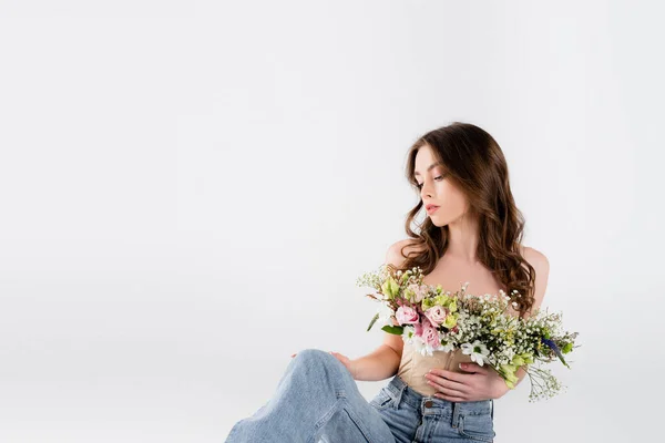 Curly woman with different flowers in blouse looking at jeans isolated on grey — Stock Photo