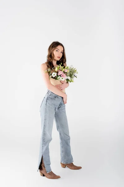 Lunghezza completa del modello elegante con fiori in camicetta guardando la fotocamera su sfondo grigio — Foto stock