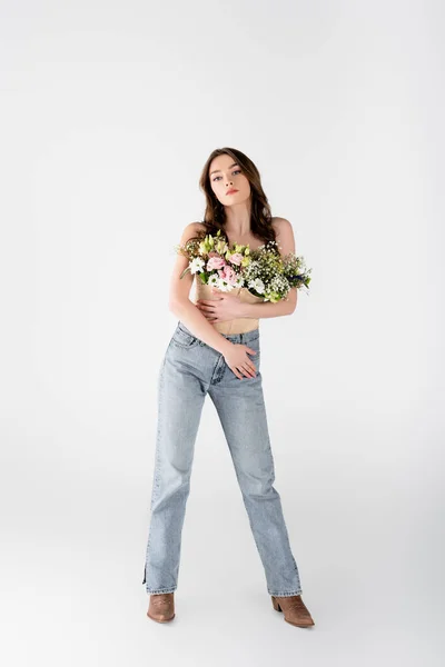 Piena lunghezza di giovane donna in jeans e fiori in camicetta in piedi su sfondo grigio — Foto stock