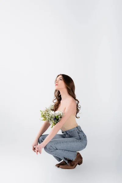 Femme élégante avec des fleurs en chemisier regardant vers le haut sur fond gris — Photo de stock
