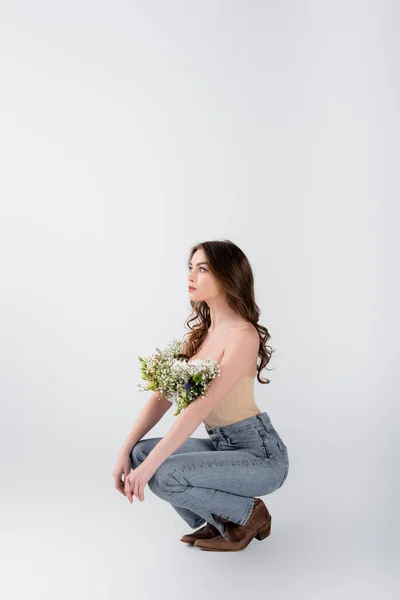 Junge Frau mit nackten Schultern und Blumen in Bluse schaut vor grauem Hintergrund weg — Stockfoto