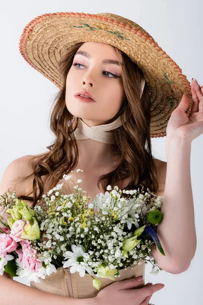 Junges Model mit Strohhut und verschiedenen Blumen in Bluse isoliert auf grau — Stockfoto