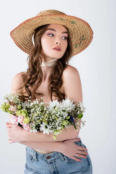 Кучерява жінка в сонячному капелюсі і квіти в блузці позує ізольовано на сірому — стокове фото