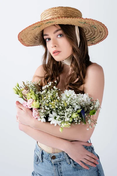 Mulher de jeans e chapéu de palha abraçando flores isoladas em cinza — Fotografia de Stock