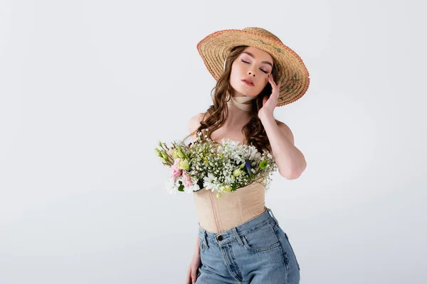 Model in jeans, sun hat and flowers in blouse posing with closed eyes isolated on grey — Stock Photo