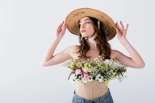Молода жінка позує з солом'яним капелюхом і квітами ізольовані на сірому — стокове фото