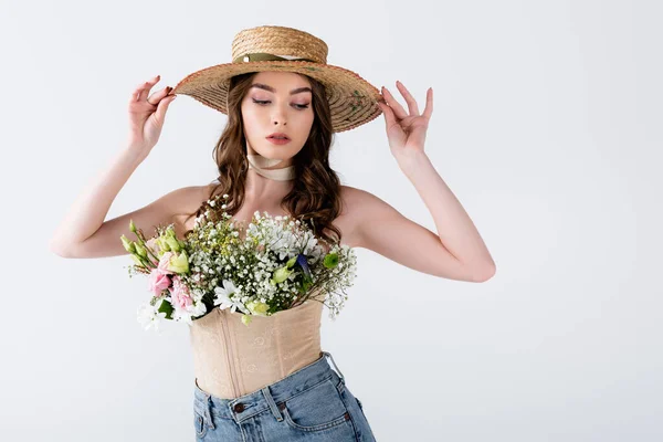 Femme tendance tenant un chapeau de soleil et posant avec différentes fleurs en chemisier isolé sur gris — Photo de stock