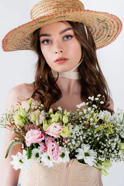 Brünette Frau mit Strohhut und Blumen blickt vereinzelt in die Kamera auf grau — Stockfoto