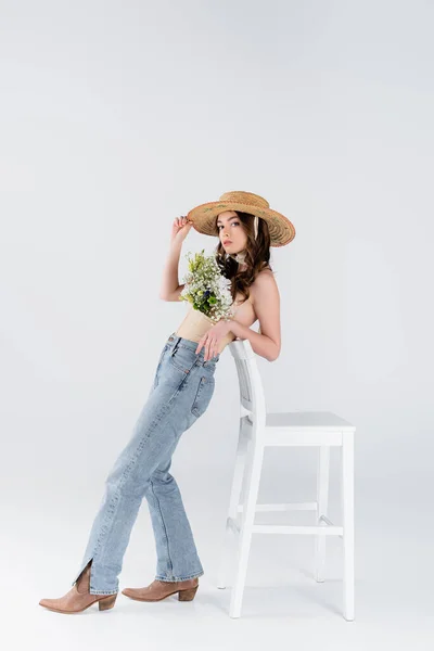Trendy model with flowers in blouse standing near chair on grey background — Stock Photo