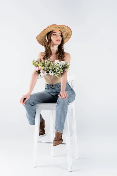 Stylish model with flowers in blouse posing on chair on grey background — Stock Photo