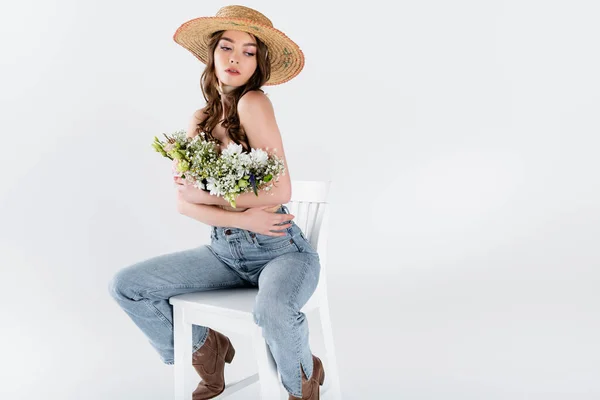 Stilvolle Frau umarmt Blumen, während sie auf Stuhl isoliert auf grau sitzt — Stockfoto