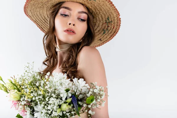 Bruna donna in cappello da sole guardando lontano vicino bouquet isolato su grigio — Foto stock