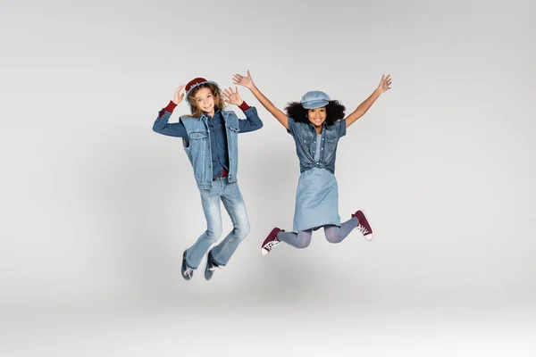 Full length view of excited multicultural girls in trendy clothes levitating on grey — Stock Photo