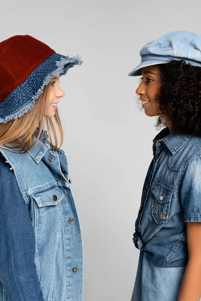 Vista lateral de alegres, amigos inter-raciais na moda sorrindo um para o outro isolado no cinza — Fotografia de Stock