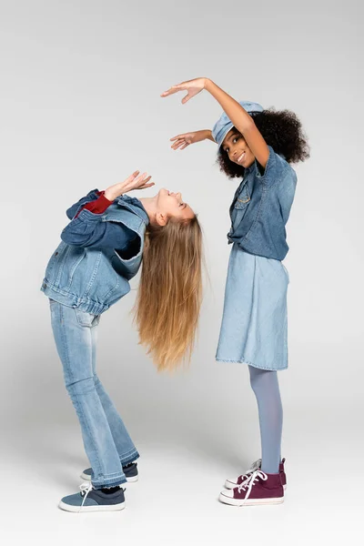 Joyful african american girl looking at camera while showing scaring gesture near friend on grey — Stock Photo