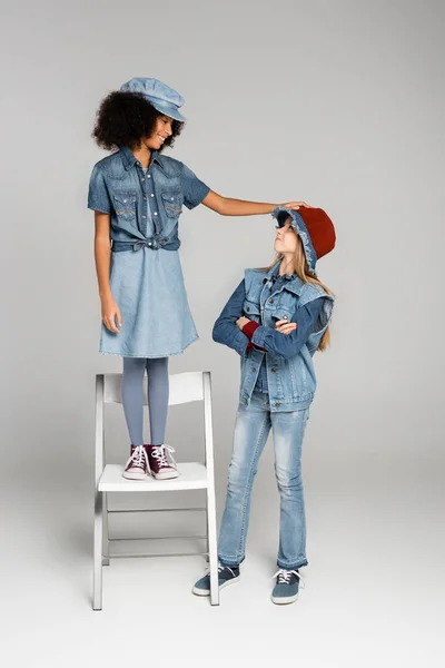 Stylish african ameican girl standing on chair near friend on grey — Stock Photo