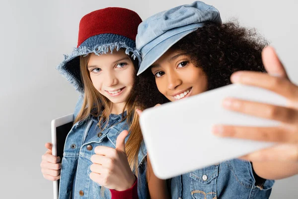 Elegante ragazza afroamericana prendendo selfie con un amico che mostra come isolato su grigio, sfocato primo piano — Foto stock