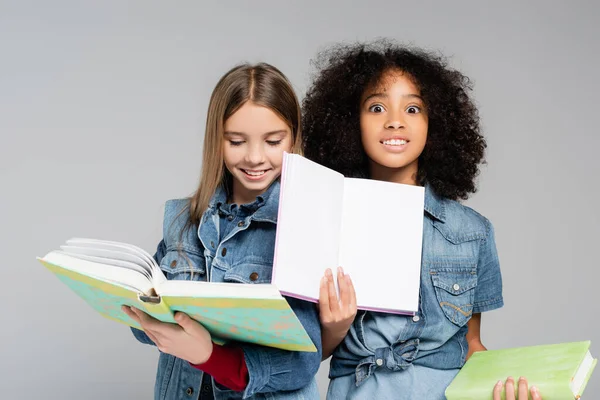 Emocionado afroamericano colegiala mostrando cuaderno en blanco cerca feliz amigo aislado en gris - foto de stock