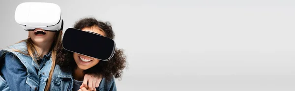 Excited interracial girls having fun in vr headsets isolated on grey, banner — Stock Photo