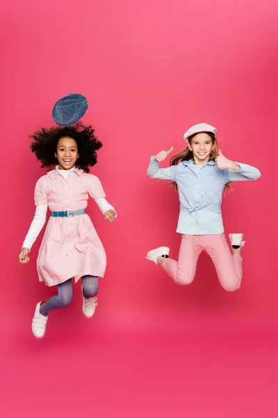 Excitado interracial niñas en elegante primavera traje levitating en rosa - foto de stock