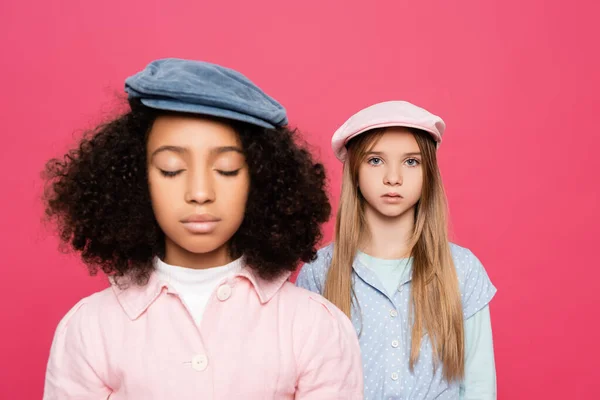 Menina da moda olhando para a câmera perto de amigo americano africano com olhos fechados isolados em rosa — Fotografia de Stock