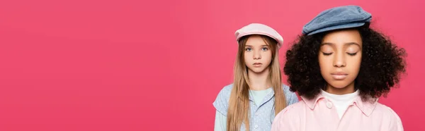 Stylish kid looking at camera near african american girl posing with closed eyes isolated on pink, banner — Stock Photo