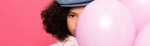 Afro americano ragazza guardando fotocamera bianco oscurante faccia con palloncini festivi isolato su rosa, banner — Foto stock