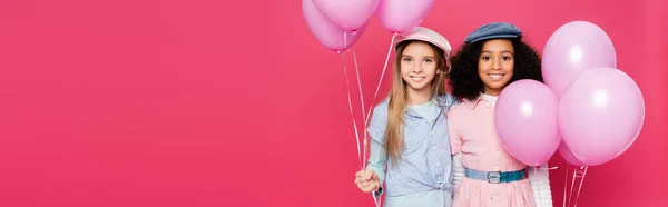 Stylish interracial kids holding festive balloons while posing isolated on pink, banner — Stock Photo