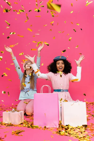 Asombrados, elegantes niños multiculturales divirtiéndose cerca de confeti y regalos en rosa - foto de stock