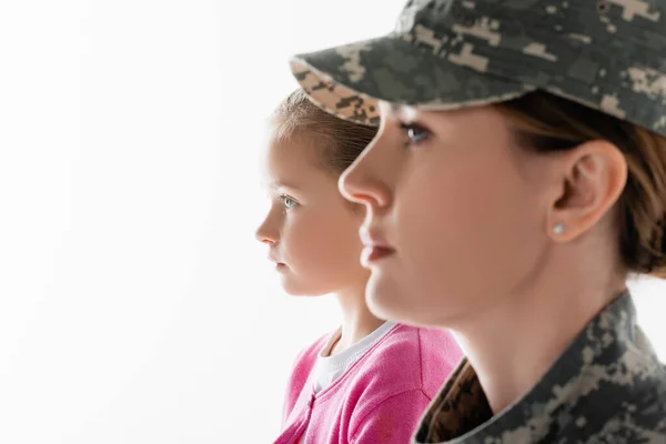 Vista lateral del niño mirando hacia otro lado cerca de la madre en uniforme militar en primer plano borroso aislado en blanco - foto de stock