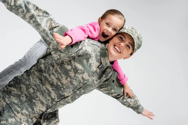 Chico excitado acariciando a la madre en uniforme militar aislado en gris - foto de stock