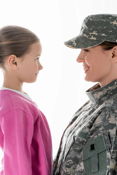 Vista lateral del niño sonriente mirando a la madre en uniforme militar aislado en blanco - foto de stock