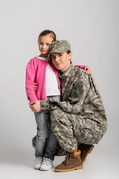 Soldado abrazando a su hija y mirando a la cámara sobre fondo gris - foto de stock