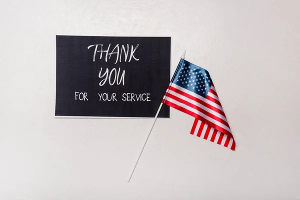 Vista superior de la tarjeta con gracias por su servicio de letras y bandera americana sobre fondo gris - foto de stock