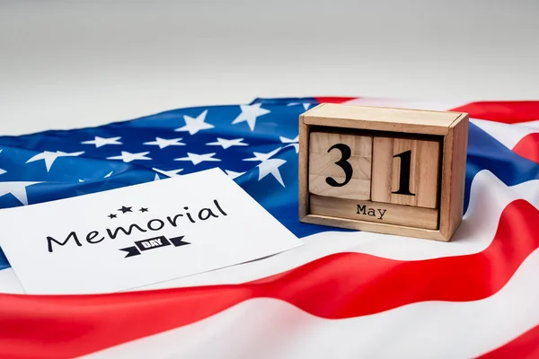 Tarjeta con letras de día conmemorativo, calendario de madera y bandera americana sobre fondo gris - foto de stock