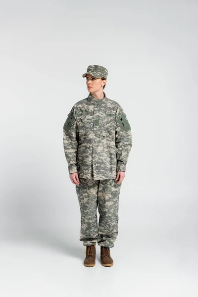 Mujer con ropa militar de pie sobre fondo gris - foto de stock
