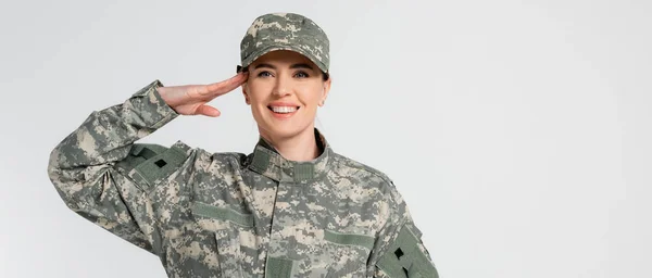 Cheerful soldier saluting and looking at camera isolated on grey, banner — Stock Photo