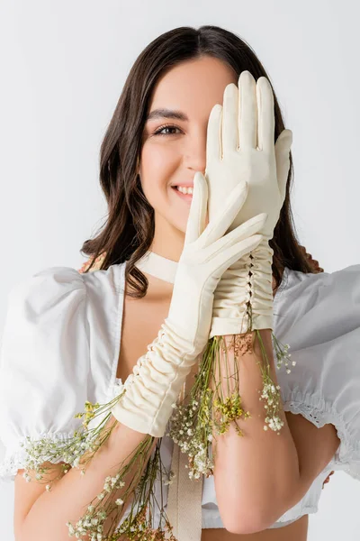 Щаслива молода жінка вкриває обличчя руками в рукавичках з квітами ізольовано на білому — стокове фото