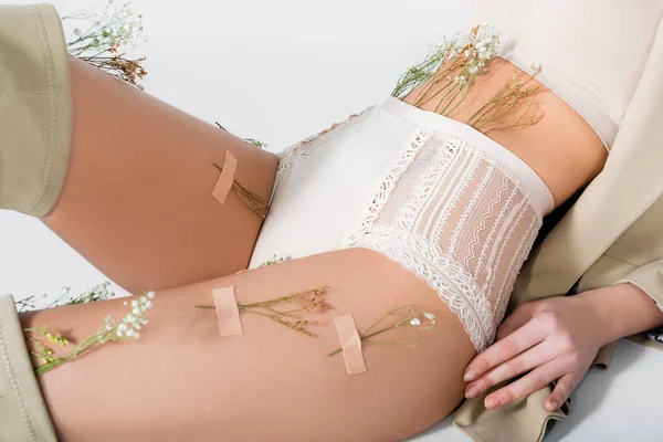 Vue recadrée du modèle en blazer, crop top et culotte avec des fleurs en fleurs couchées tout en posant isolé sur blanc — Photo de stock