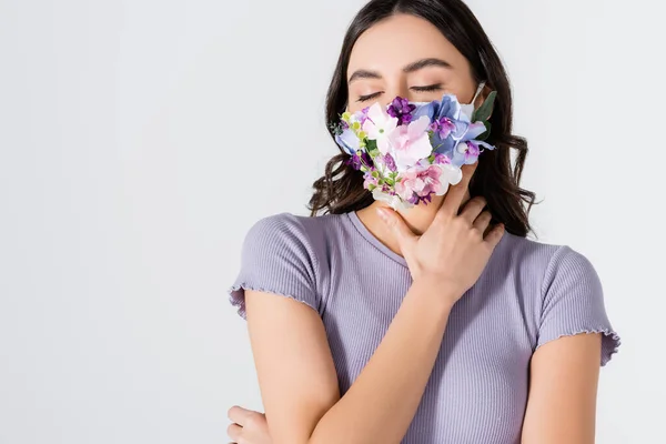 Modelo joven en la parte superior de la cosecha y máscara médica con flores en flor posando aislado en blanco - foto de stock