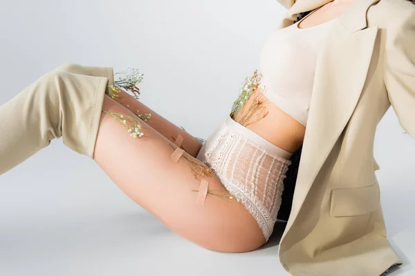 Vue recadrée du modèle en blazer, crop top et culotte avec des fleurs en fleurs assis tout en posant sur blanc — Photo de stock