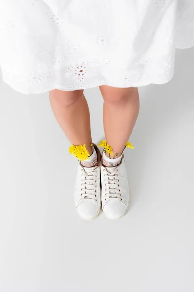 High angle view of model in sneakers with yellow spring wildflowers posing on white — Stock Photo