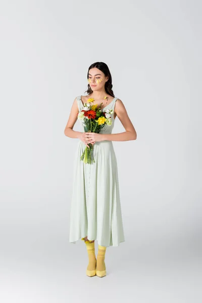 Full length of young woman with petals on face holding bouquet of flowers isolated on white — Stock Photo